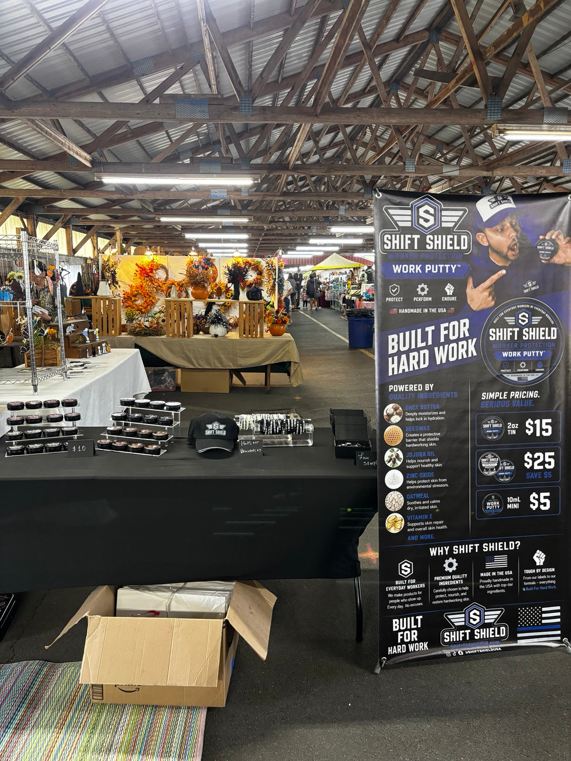 Shift Shield craft show booth with tiered Work Putty displays, a branded hat, bracelets, samples and a tall banner.